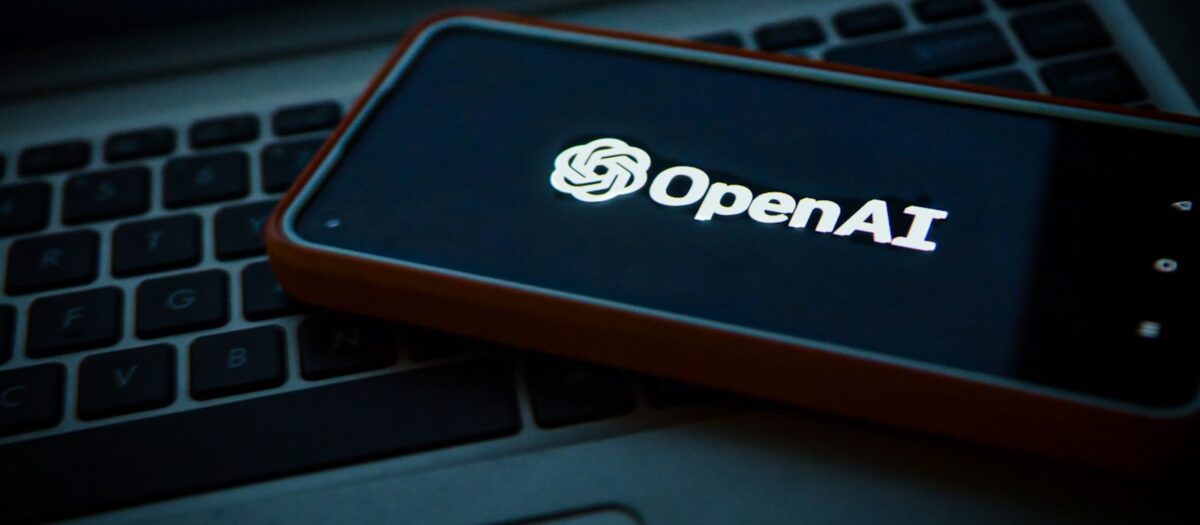 노트북 키보드 위에 놓인 스마트폰 화면에서 환하게 빛나는 OpenAI 로고