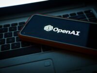 노트북 키보드 위에 놓인 스마트폰 화면에서 환하게 빛나는 OpenAI 로고